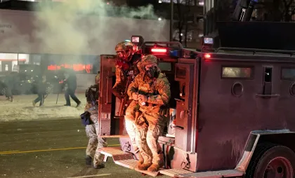 Un agent al Poliției de Frontieră a SUA trage cuiul unei fumigene înainte de a o arunca către protestatarii adunați în fața unui hotel din Minneapolis