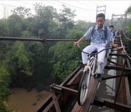 Cel mai periculos drum spre scoala: Copiii merg cu bicicleta pe scandurile de lemn ale unui pod suspendat Cel mai periculos drum spre scoala: Copiii merg cu bicicleta pe scandurile de lemn ale unui pod suspendat